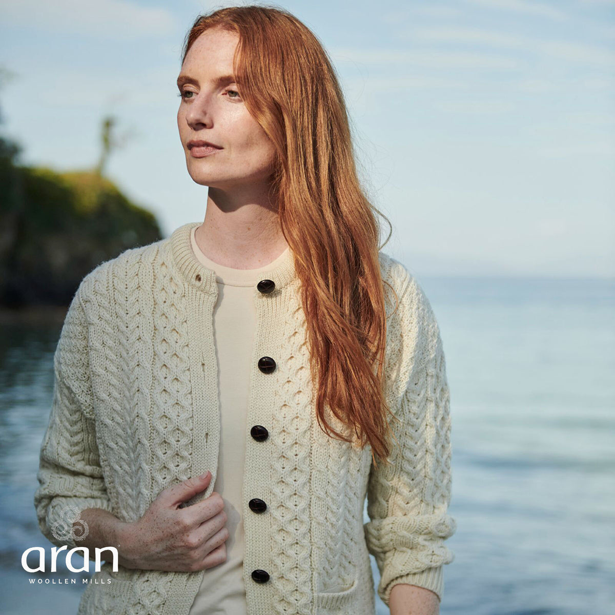 Woman with long red hair wearing cream knit cardigan by water