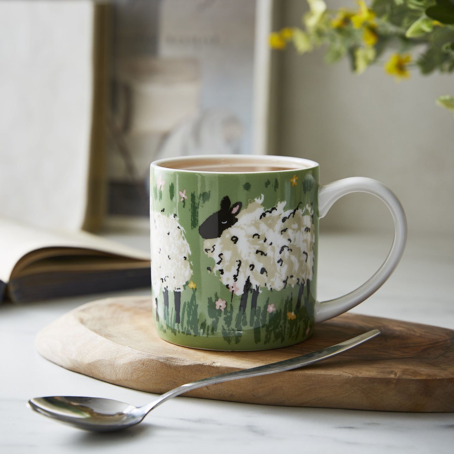 Green mug with sheep illustrations filled with coffee on wooden board