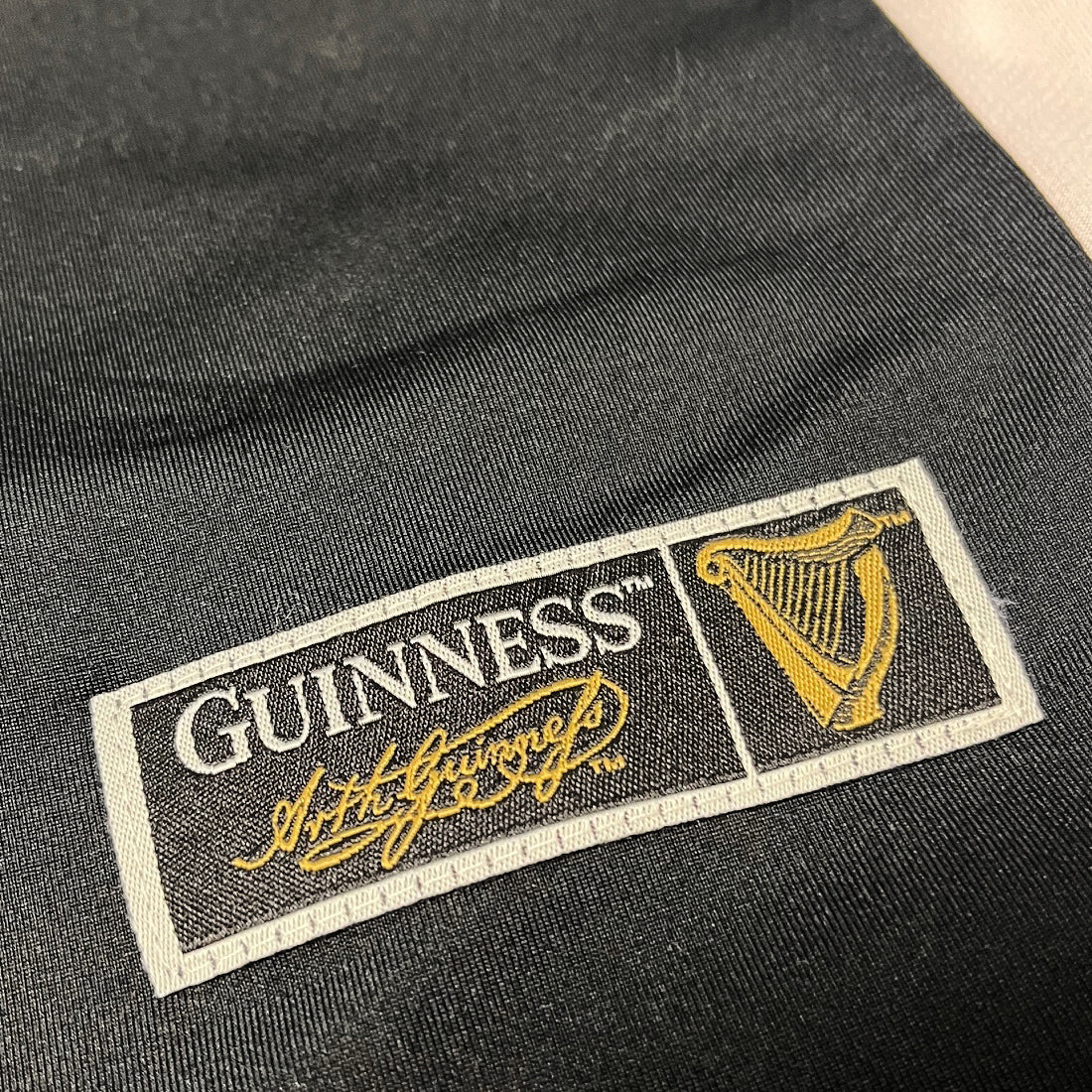 Black fabric with a stitched Guinness logo patch featuring a harp