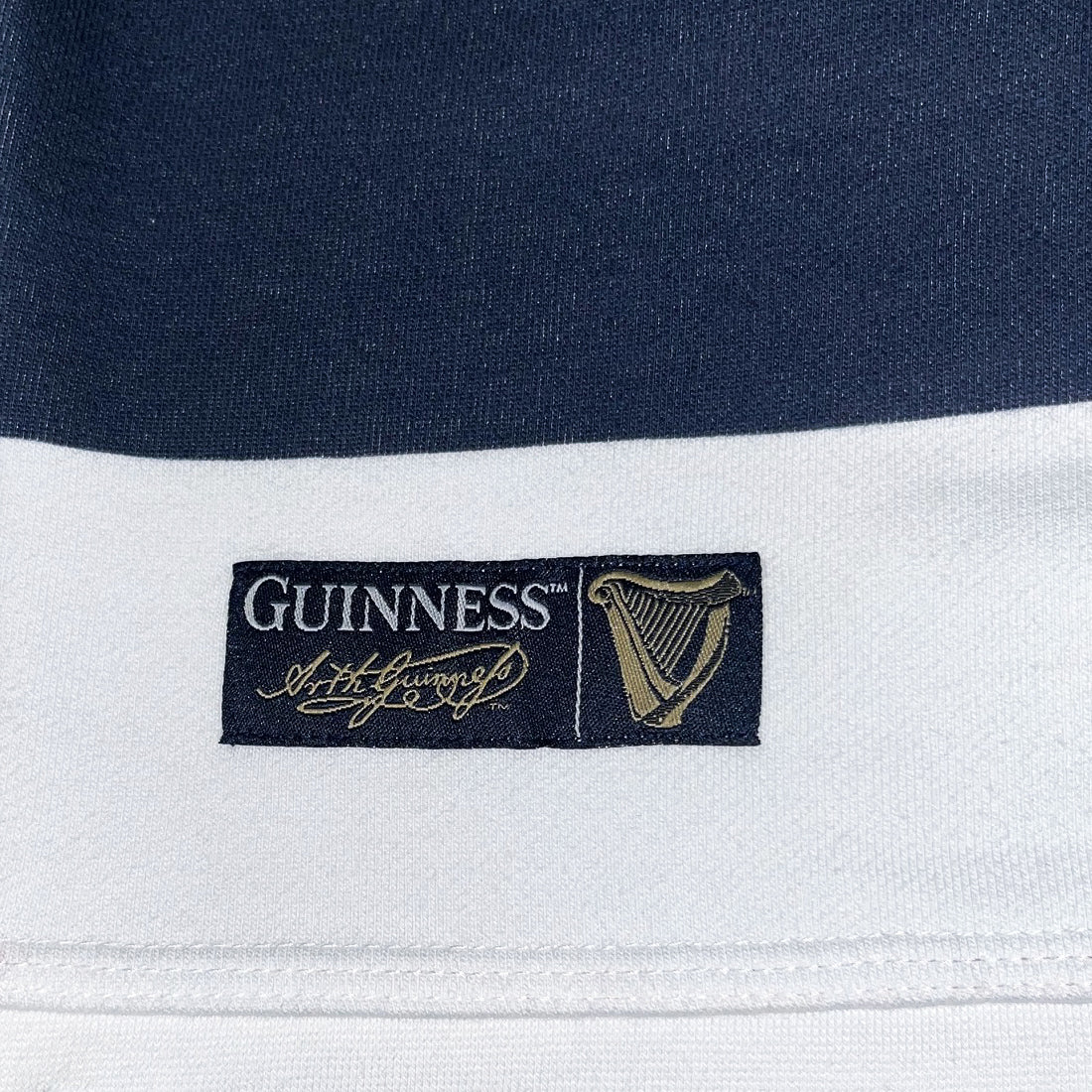 Guinness label patch with the logo and gold harp emblem on the navy and white rugby sweatshirt