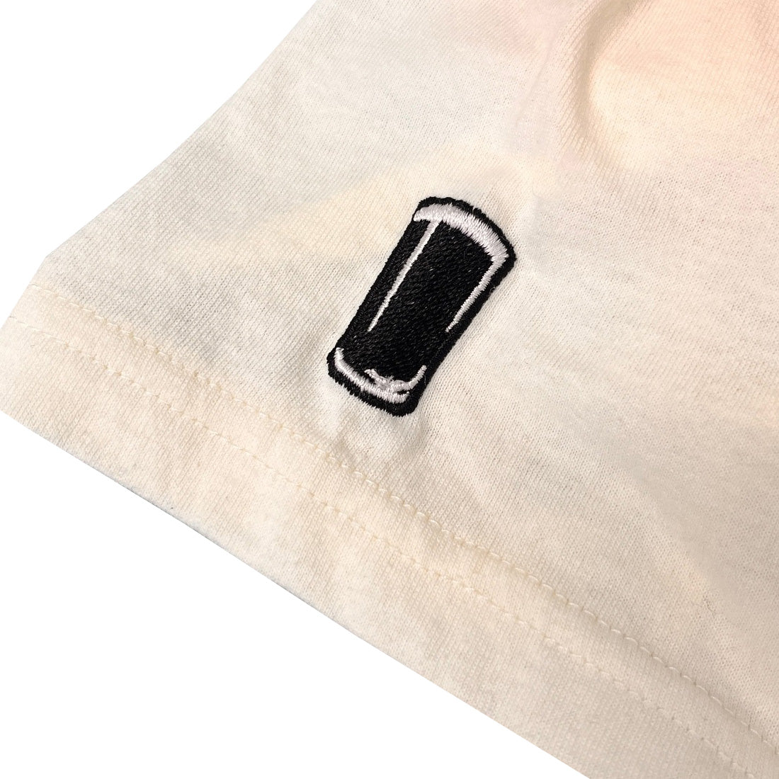 Close up of cream T shirt sleeve with black embroidered patch