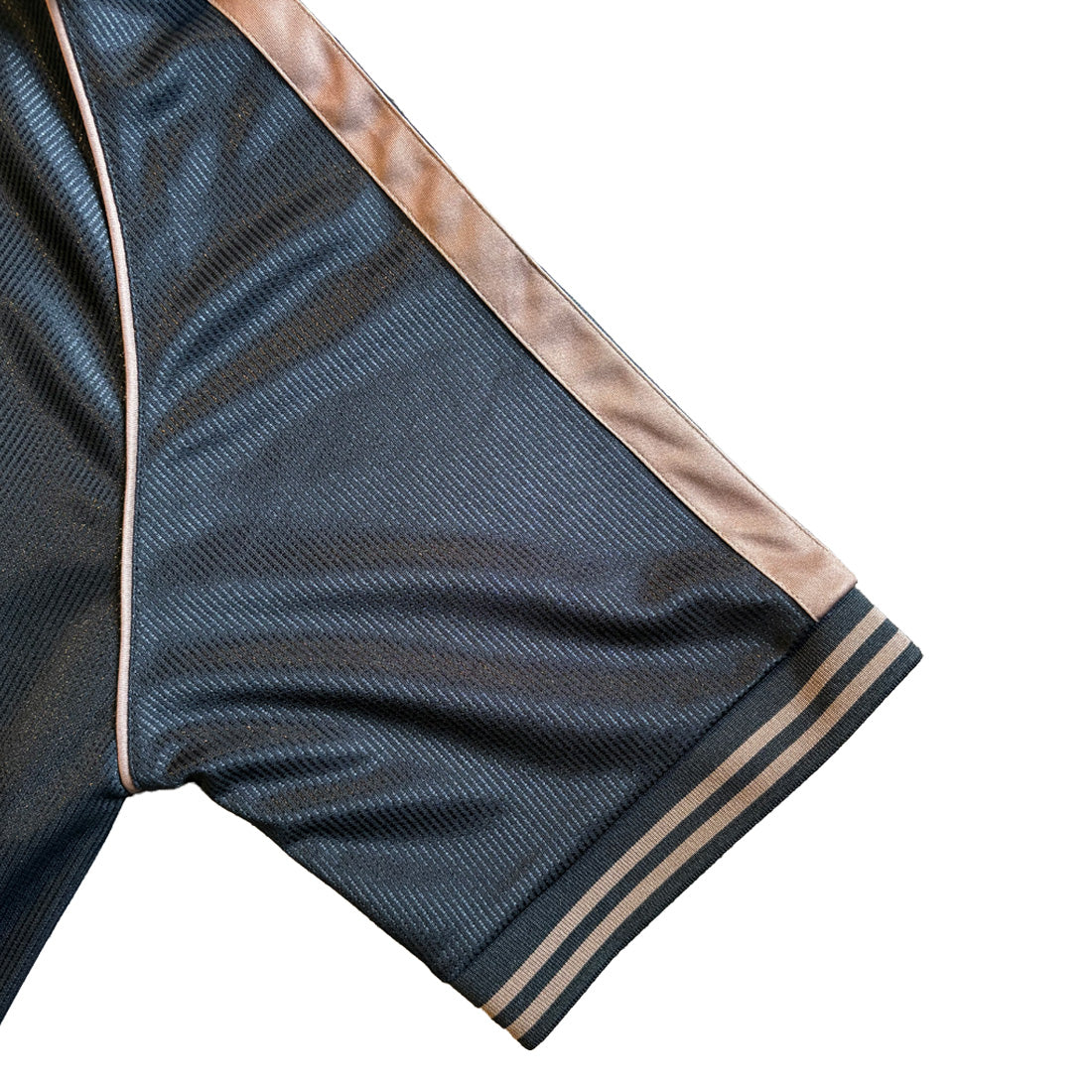 Close-up of dark navy football top fabric with brown piping along the seam and striped cuff.