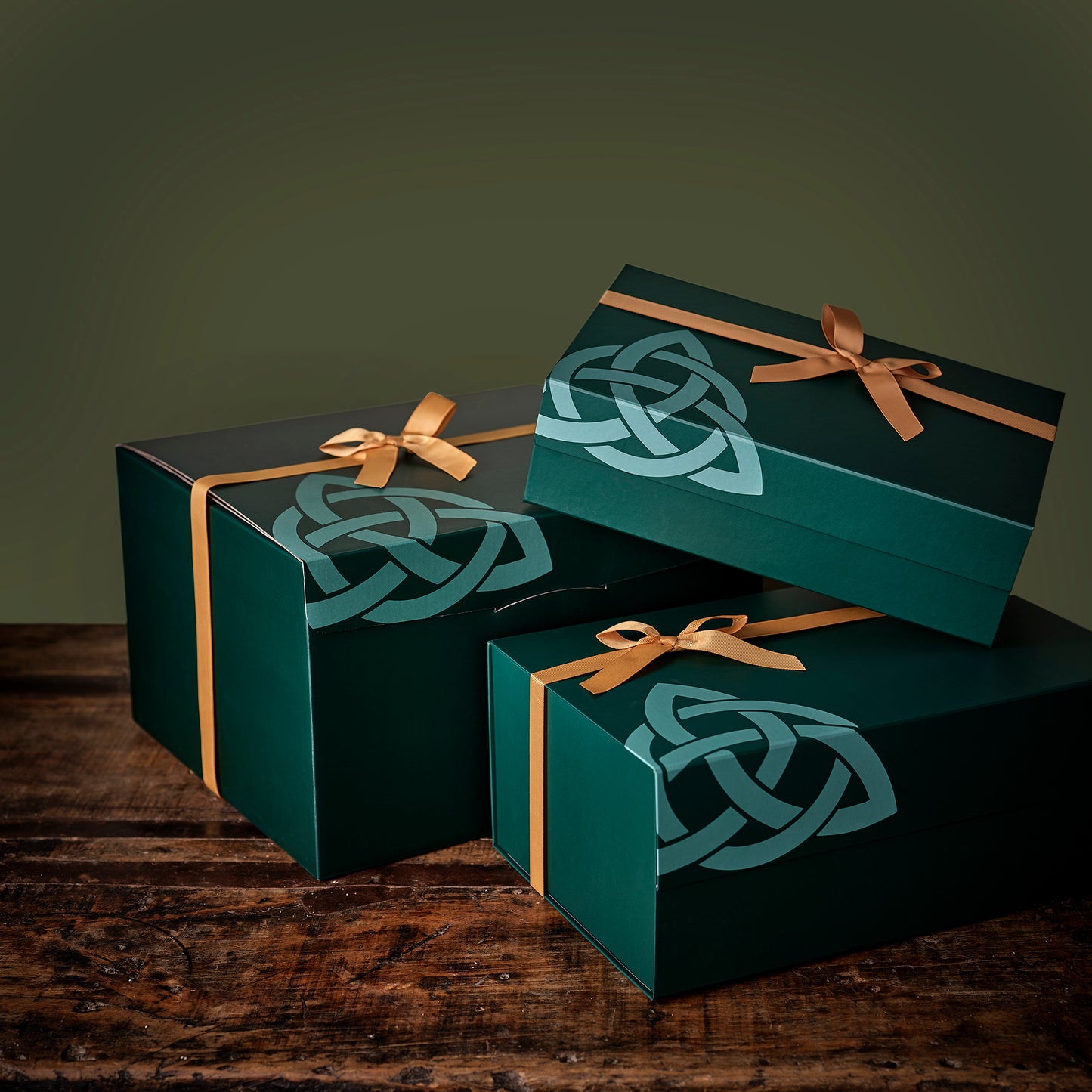 Three dark green gift boxes with gold ribbons and Celtic knot designs