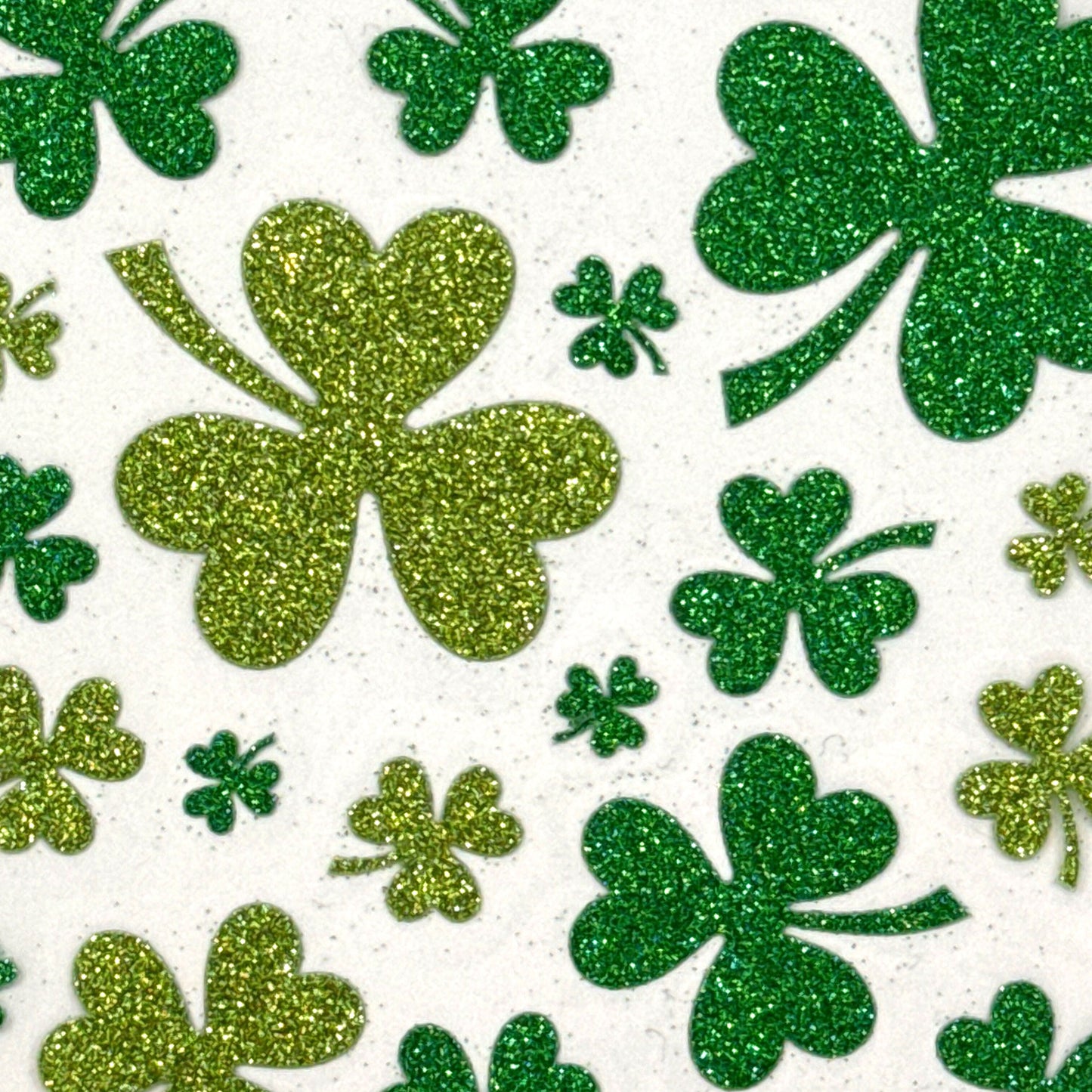 Green and gold glittery shamrocks scattered on a white background