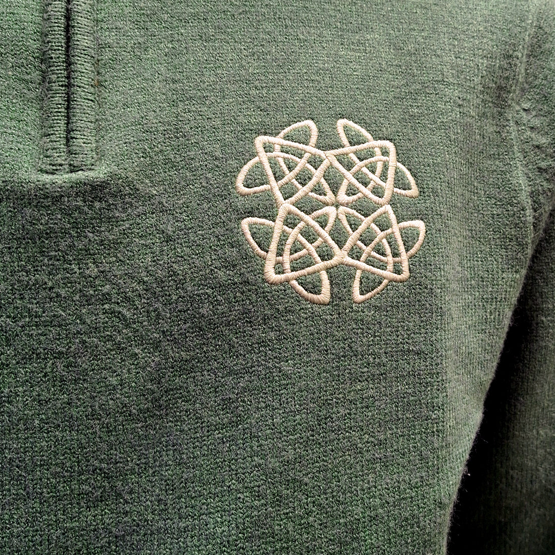 Close-up of white Celtic knot embroidery on the chest of a sage green jumper
