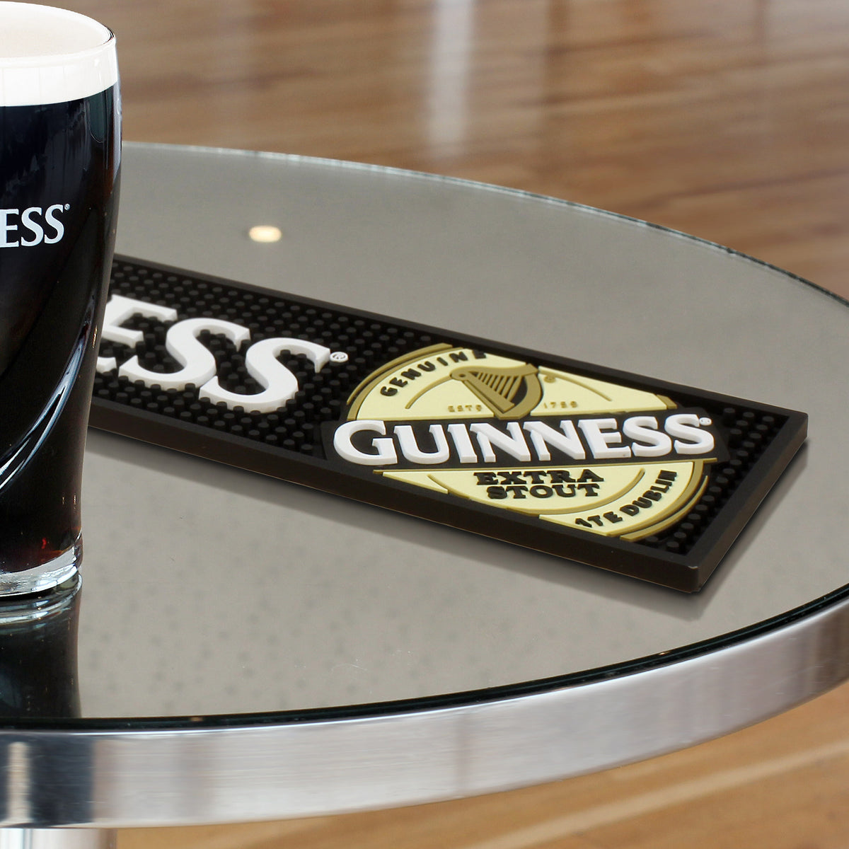 Partially visible pint of dark stout beer on glass table with Guinness mat