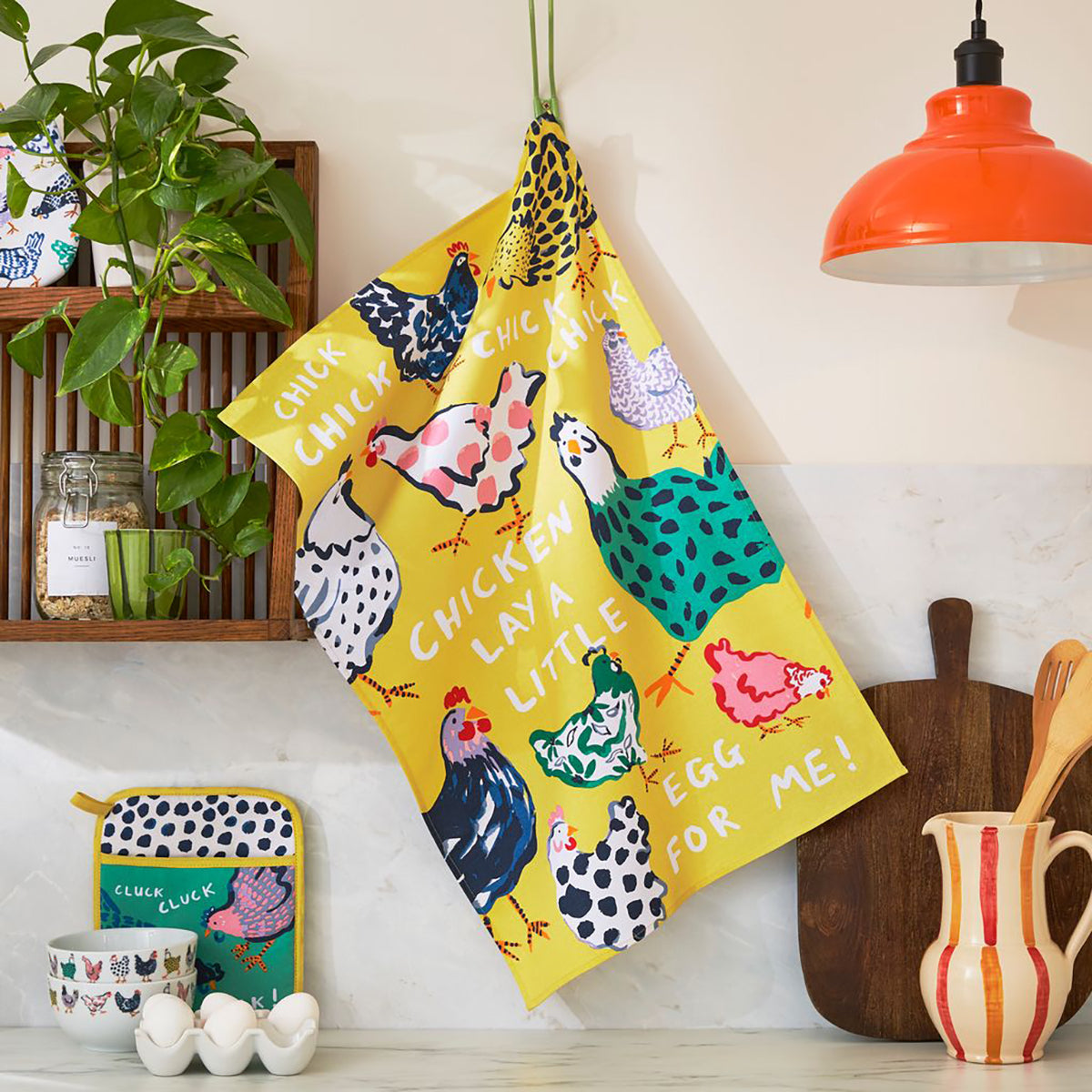 Chick Chicken cotton tea towel with bright yellow background hung diagonally in a kitchen beside plants and cookware