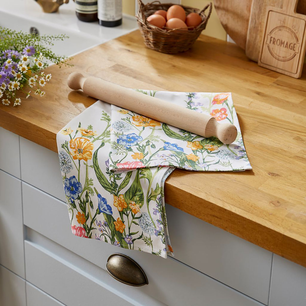 Floral Cottage Garden cotton tea towel laid over a wooden kitchen counter with a rolling pin.