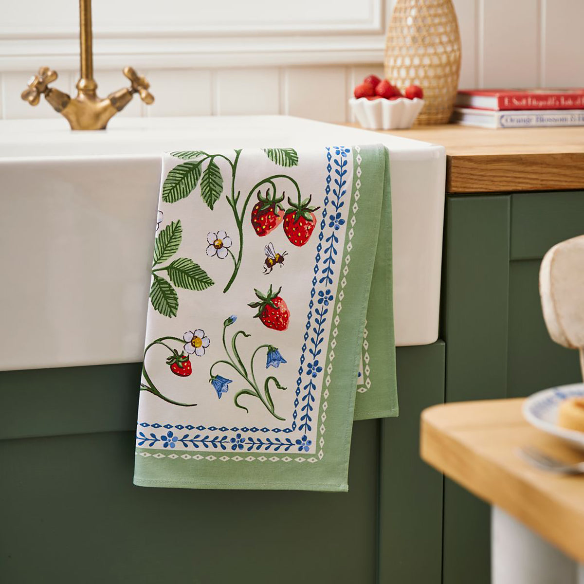 Strawberry Patch Cotton Tea Towel with green border draped over a kitchen sink