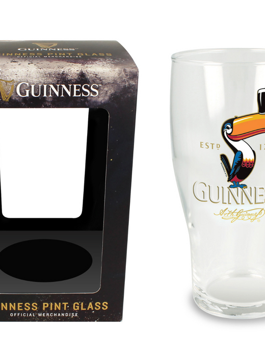 Clear pint glass with colorful toucan and Guinness logo beside black packaging box