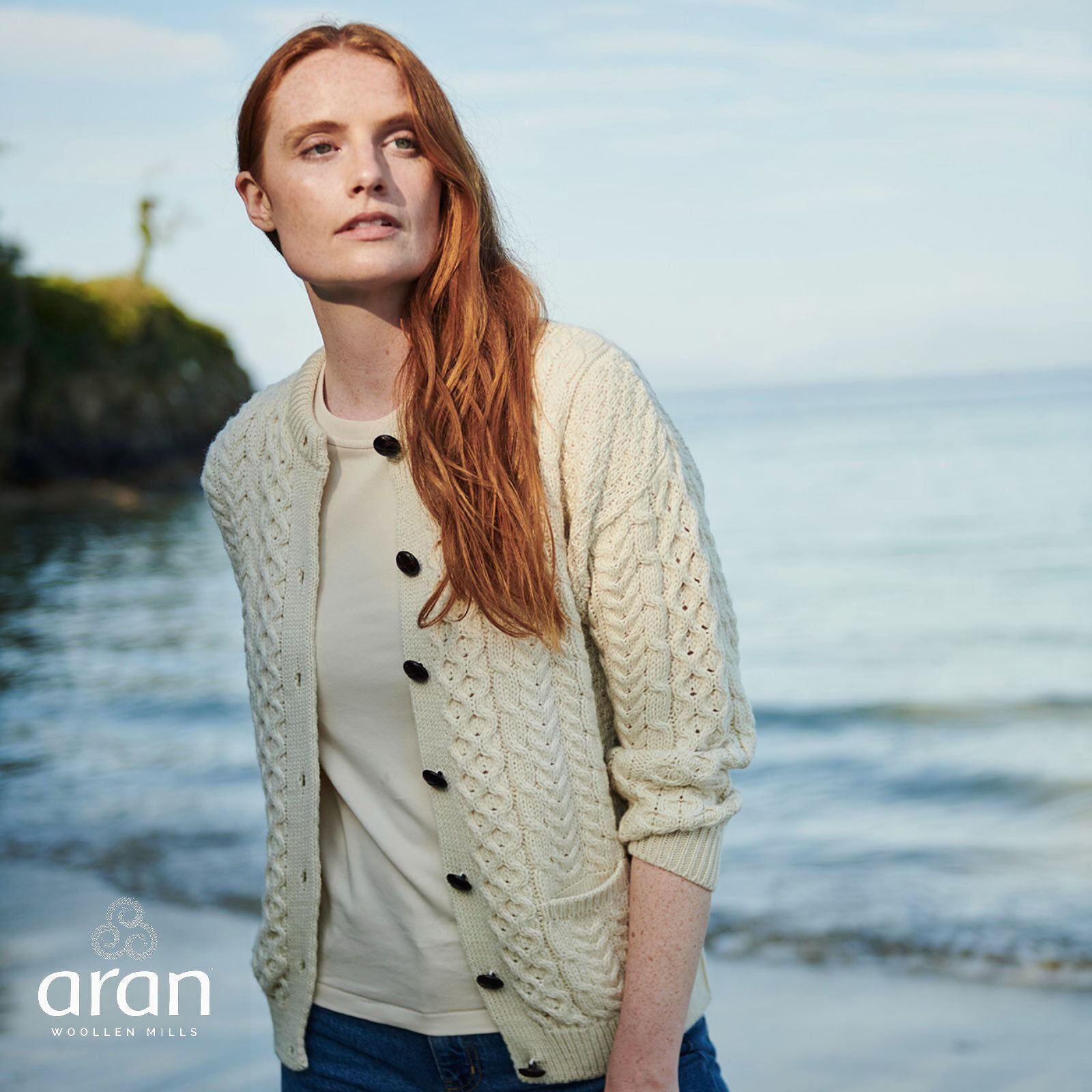 Woman with red hair wearing cream cable knit cardigan by the sea