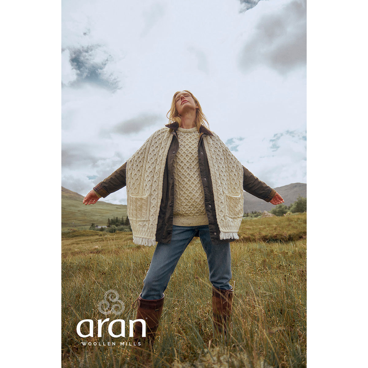 Woman wearing a cream cable knit Shannon Throwover Merino Aran Wrap outdoors in a field