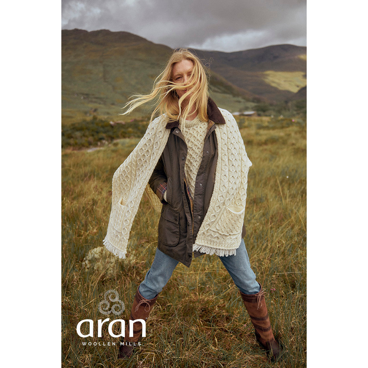 Model wearing cream Shannon Merino Aran wrap over a jacket in a windswept countryside setting.