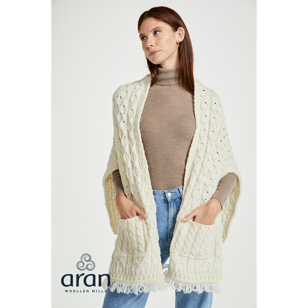 Model wearing cream Shannon Merino Aran wrap draped over shoulders with beige turtleneck and jeans in studio.