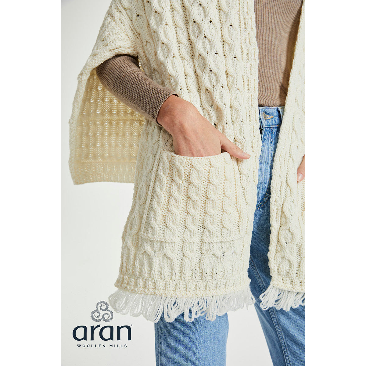 Close up of the cream Shannon Throwover Merino Aran wrap showing pocket and fringed hem worn with jeans