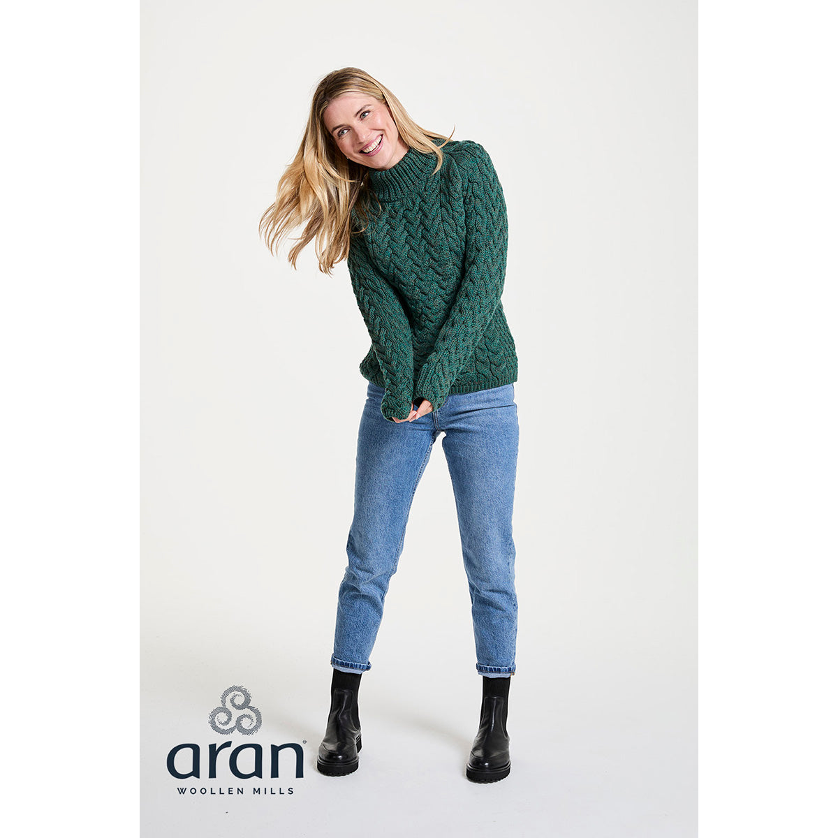 Full length shot of a woman in a green Knightstown merino aran crew sweater with jeans and boots