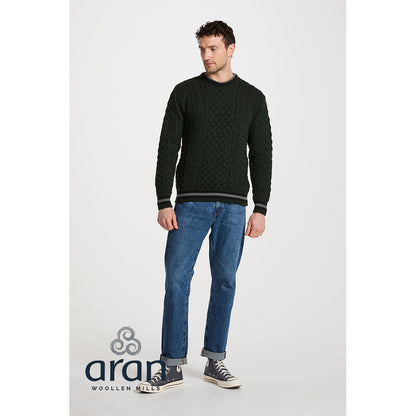 Full body shot of model in dark green Aran crewneck sweater with striped cuffs and hem, paired with jeans.