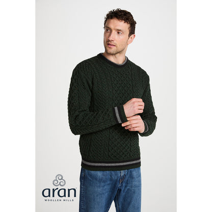 Front view of a male model wearing a dark green Inishbeg Stripe Crewneck Merino Aran sweater