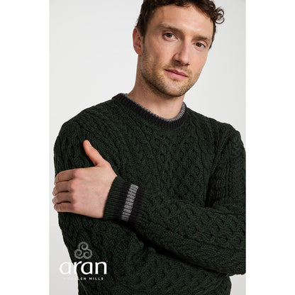 Model wearing dark green cable knit Aran sweater with striped cuffs and crew neck.