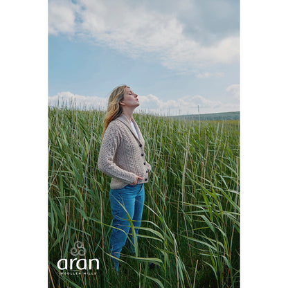 Model wearing beige Tourmakeady shawl collar Merino Aran cardigan in a sunlit field