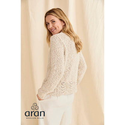 Back view of a woman in a cream knit sweater with a lace hem against a beige backdrop.