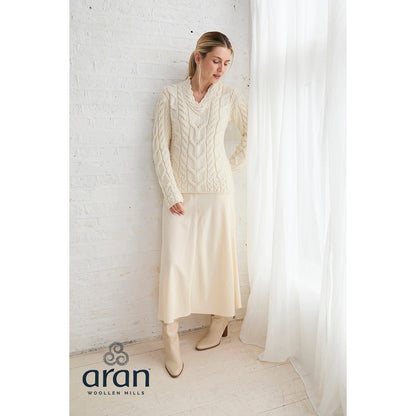 Model wearing cream Tralee Merino sweater with a matching skirt and knee high boots by a window