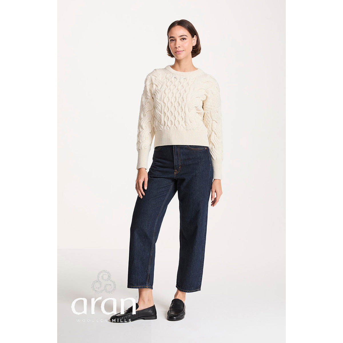 Full length view of a model wearing cream cropped cable knit jumper with dark jeans