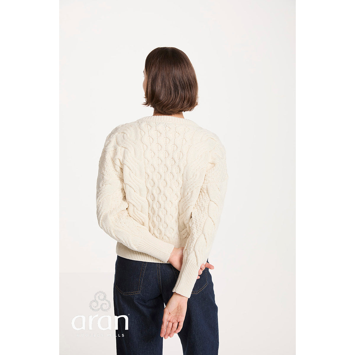 Back view of a model wearing a cropped beige cable knit jumper