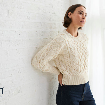 Model in cream cropped cable knit jumper posed against a white brick wall