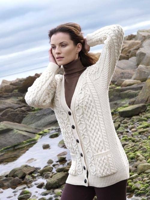 Model wearing Ladies Aran Natural Boyfriend Cardigan over a brown turtleneck beside the coast.