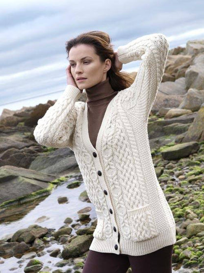 Model wearing Ladies Aran Natural Boyfriend Cardigan over a brown turtleneck beside the coast.