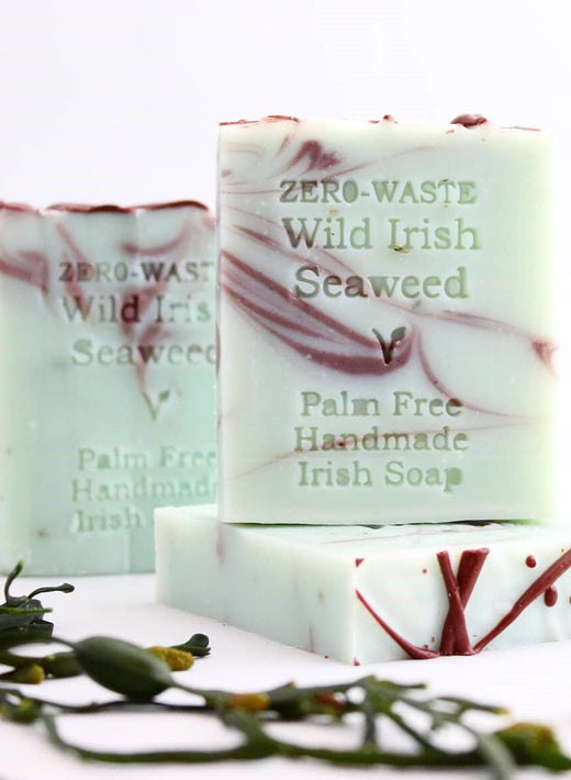 Three bars of handmade soap with marbled red and white design and seaweed nearby