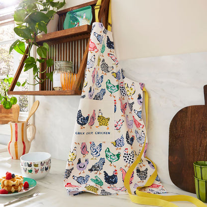 Cotton apron with colorful chicken prints and yellow trim hanging on a wooden rack in a bright kitchen