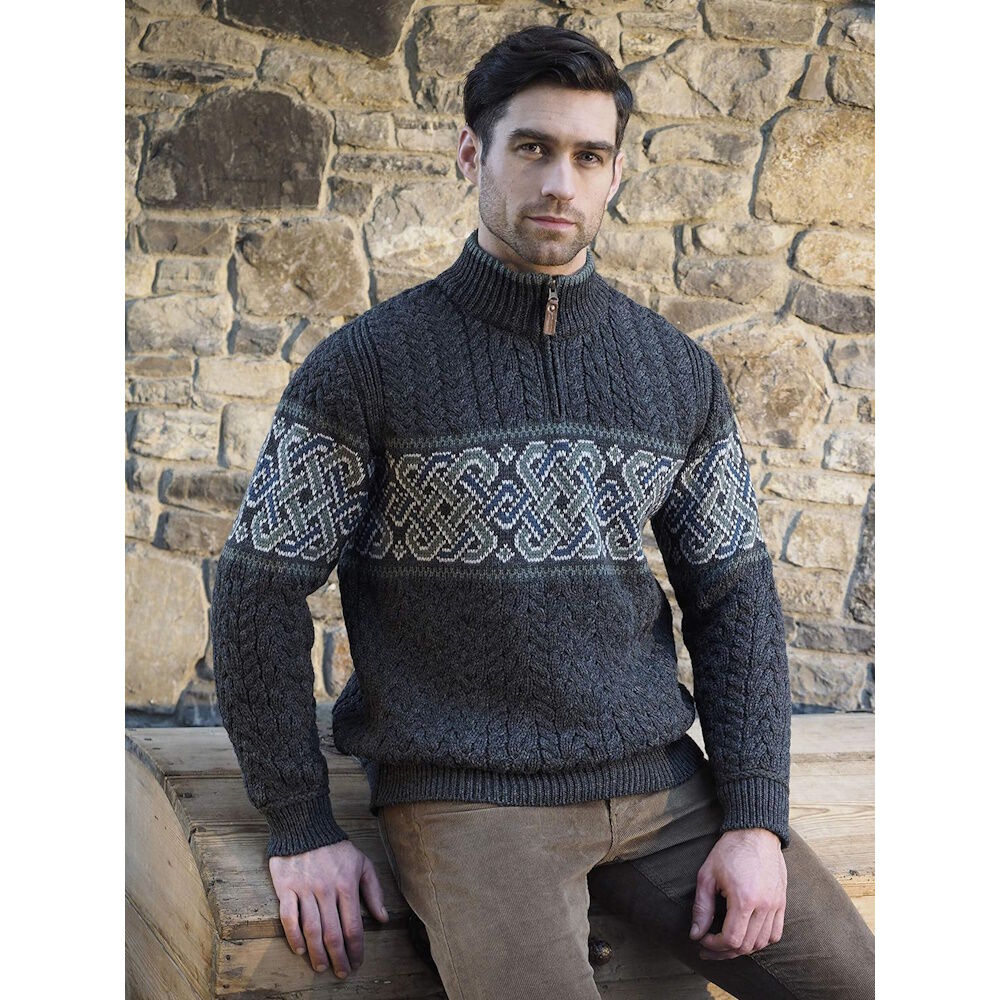 Man wearing dark gray patterned knit sweater sitting against stone wall