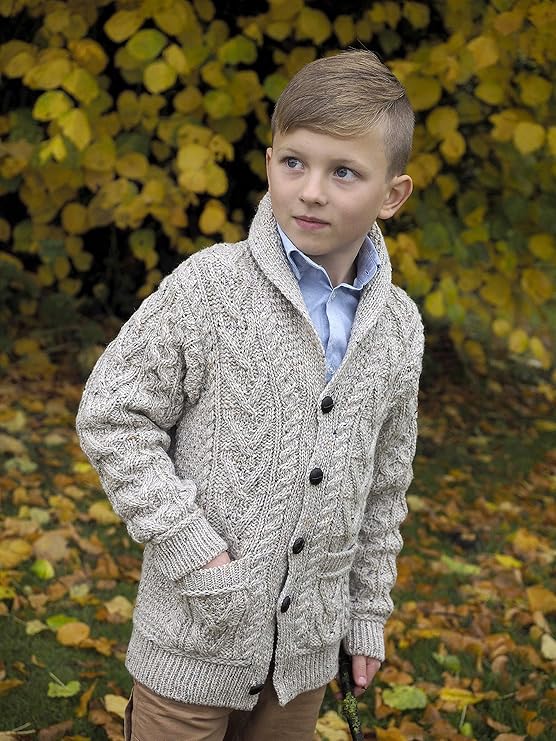 Young boy wearing a knitted cardigan standing outdoors with autumn leaves 