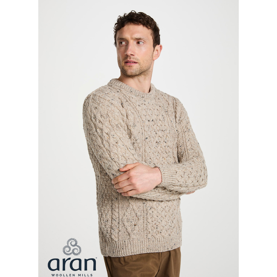Man wearing beige cable knit sweater looking to the side with arms crossed