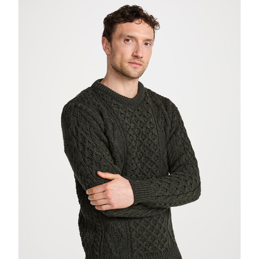 Man with short curly hair wearing dark green cable knit sweater