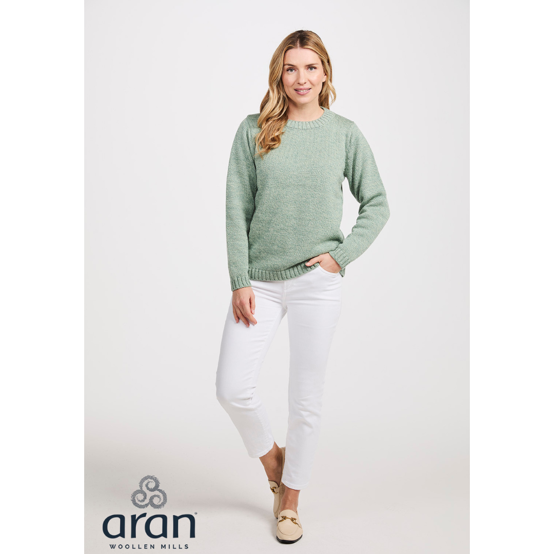 Woman wearing light green sweater and white pants standing with hand in pocket