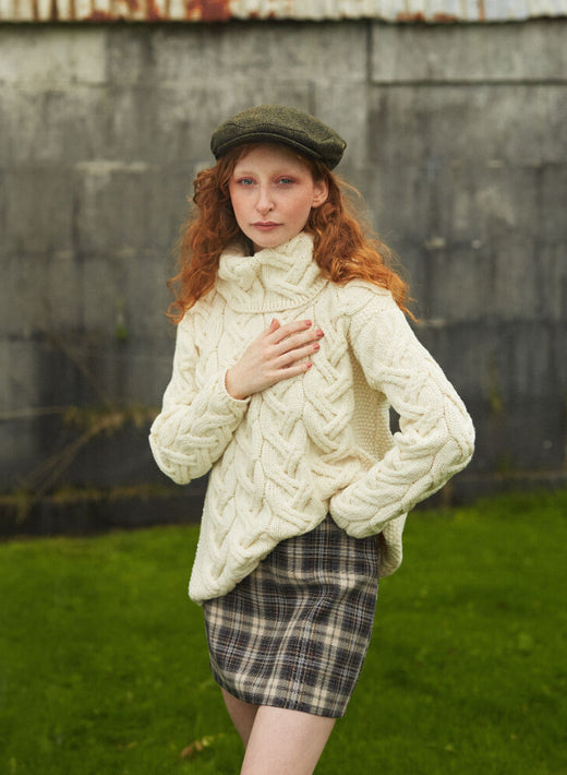 Woman with red hair wearing a cream cable knit sweater and plaid skirt