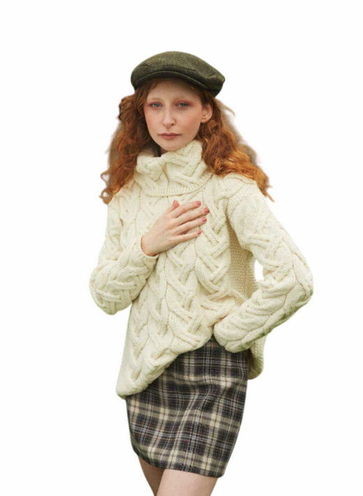 Woman with red hair wearing a cream cable knit sweater and plaid skirt