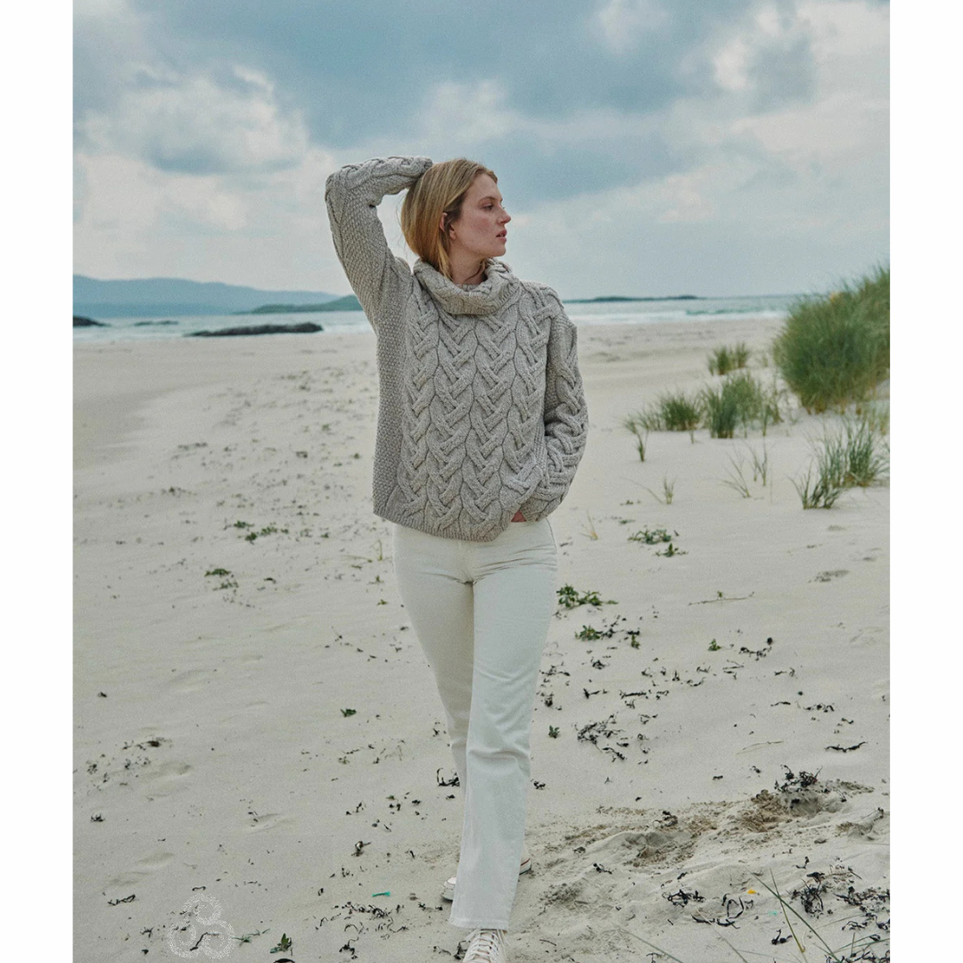 Woman in gray cable knit sweater and white pants standing on sandy beach