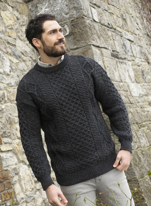 Man wearing dark gray cable knit sweater standing by stone wall