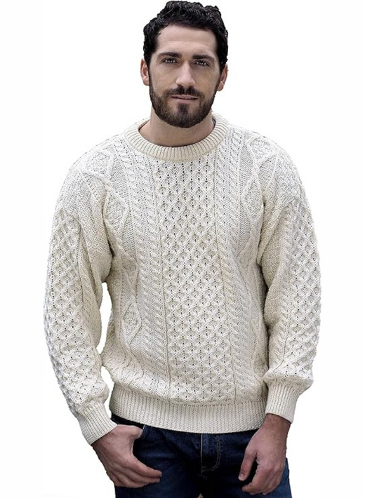 Man wearing a cream cable knit sweater and dark jeans standing