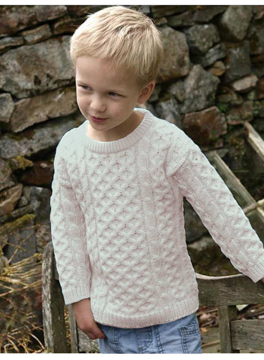 Young boy wearing a white cable knit sweater outdoors near stone wall