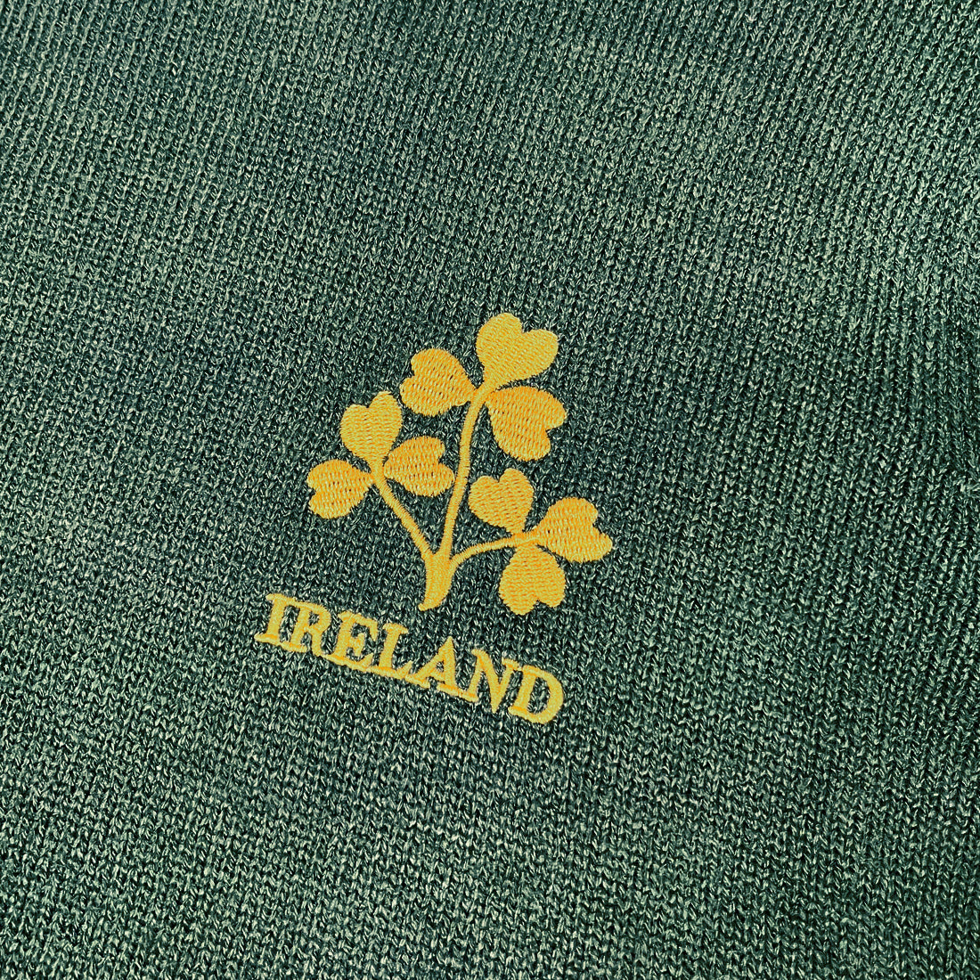 Close up of bottle green knit fabric featuring a yellow shamrock emblem and IRELAND text