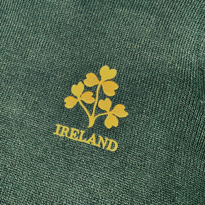Close up of bottle green knit fabric featuring a yellow shamrock emblem and IRELAND text