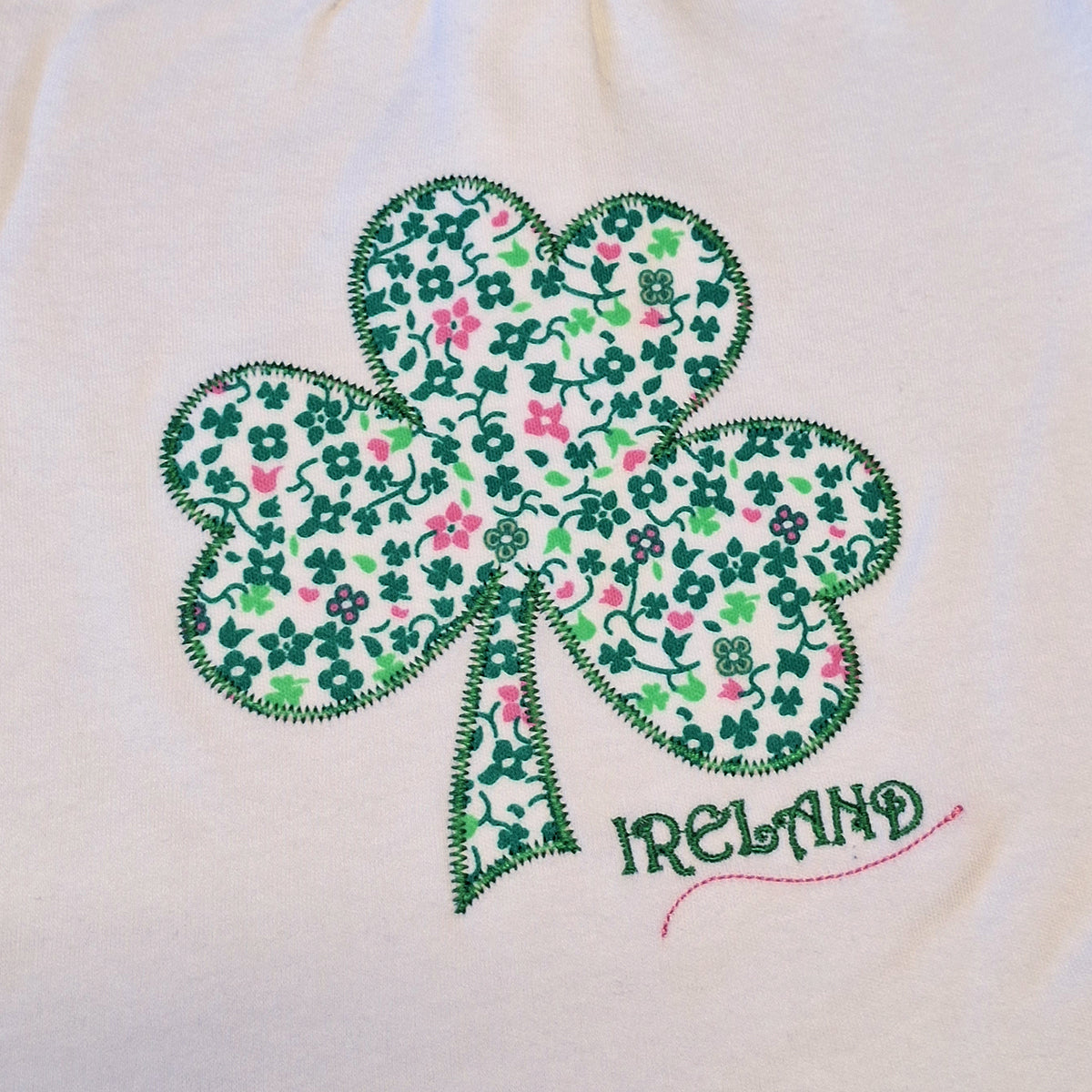 Close up of white fabric featuring a green floral shamrock applique and IRELAND stitched text