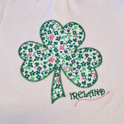 Close up of white fabric featuring a green floral shamrock applique and IRELAND stitched text