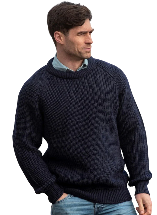 Man wearing a dark blue knitted sweater and light blue jeans looking sideways