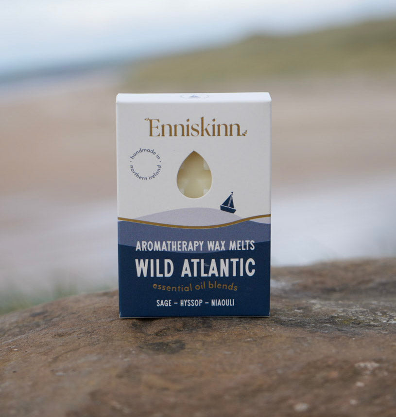 Enniskinn Wild Atlantic Aromatherapy Wax Melts box placed on a rocky beach with a blurred shoreline